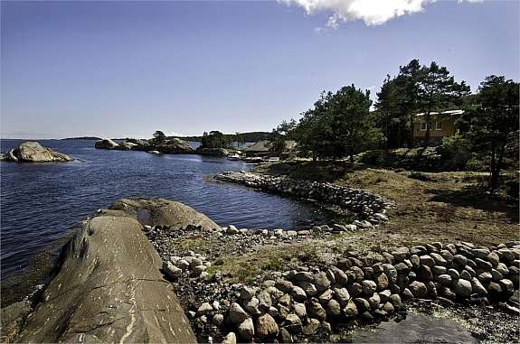 Badeskjær med rullesteinsmur og båthus i bakgrunnen Galleribilde