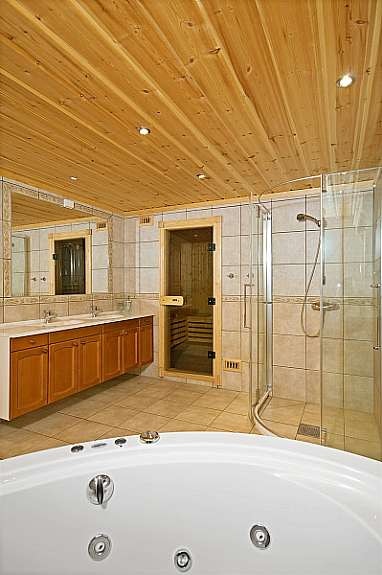 Romslig bad med fliser på gulv og vegg. Stort veggmontert speil med innredning og dobbel vask. boblebadekar, dusjhjørne, wc og badstue. Galleribilde