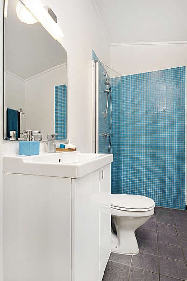 Bad med toalett, fliser i dusj hjørnet og buet glassdør. Galleribilde