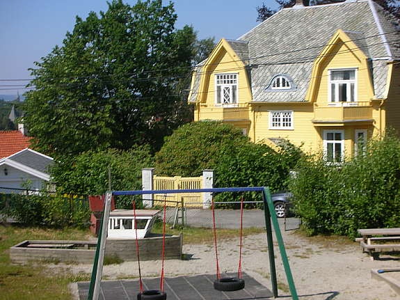 Sommerbilde av huset med lekeplassen Galleribilde