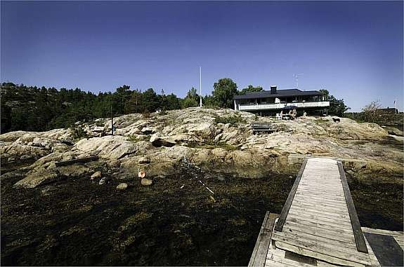 Hovedhytta sett fra flytebryggen. Sandstrand til høyre for bildet Galleribilde