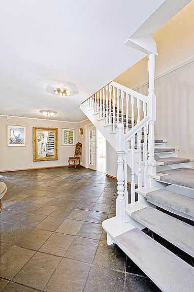 Romslig hall med skiferflis på gulvet (varmekabler) og intertrapp til 2. etasje. Galleribilde