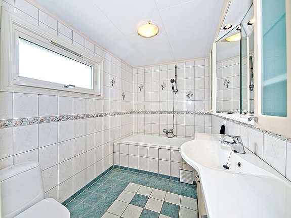 Flislagt bad med stor baderomsinnredning, gulvvarme, wc og innfliset badekar med dusj Galleribilde