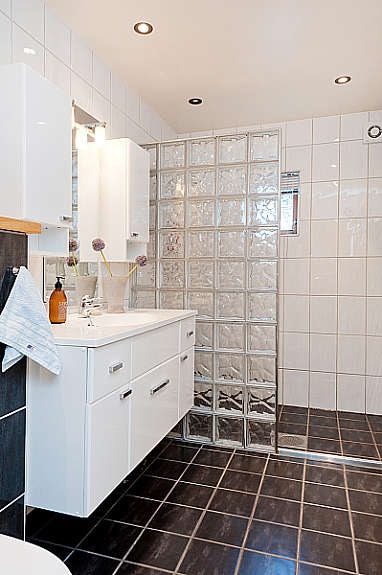 Tiltalende flislagt bad. Hvit høyglans innredning med heldekkende servant. Dusjvegg med glassbyggerstein Galleribilde