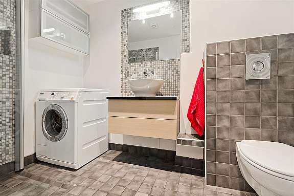 Lekkert flislagt bad med varmekabler. Innredning med lyse fronter i heltre eik, speil og belysning. Galleribilde