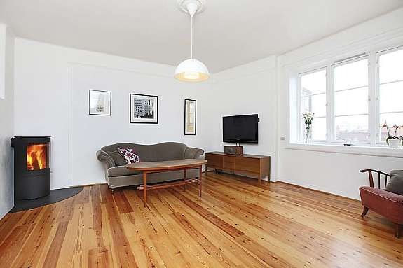 Stor, lys stue med pene gulvflater, store vindusflater og vedovn Galleribilde