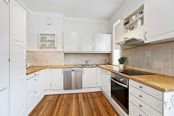 Lyst kjøkken med god skap- og benkplass, parkett på gulv, fliser over benk. Galleribilde