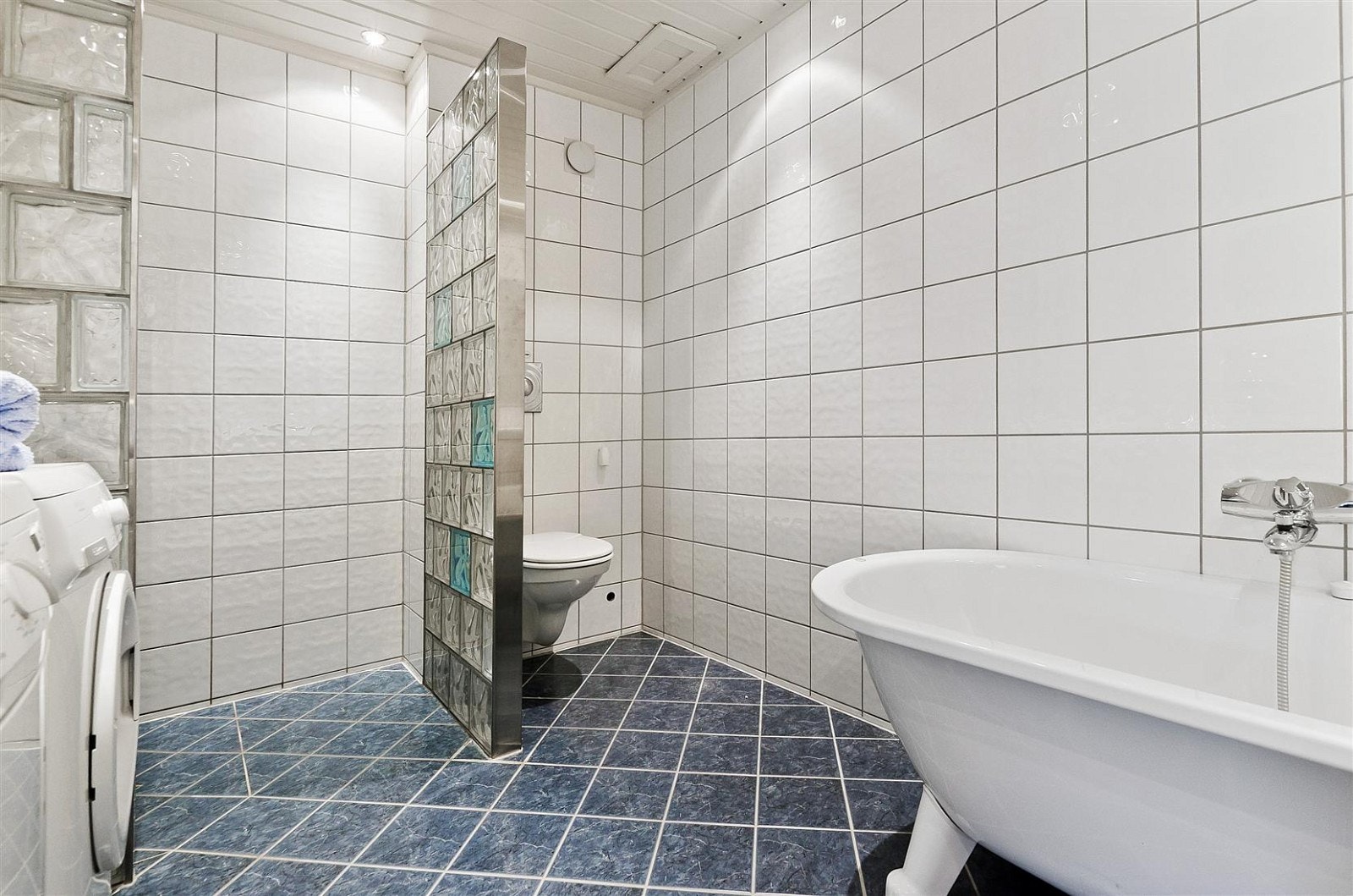 Stort bad med dusj i hjørne og badekar. Opplegg for vaskemaskin og tørketrommel. Galleribilde