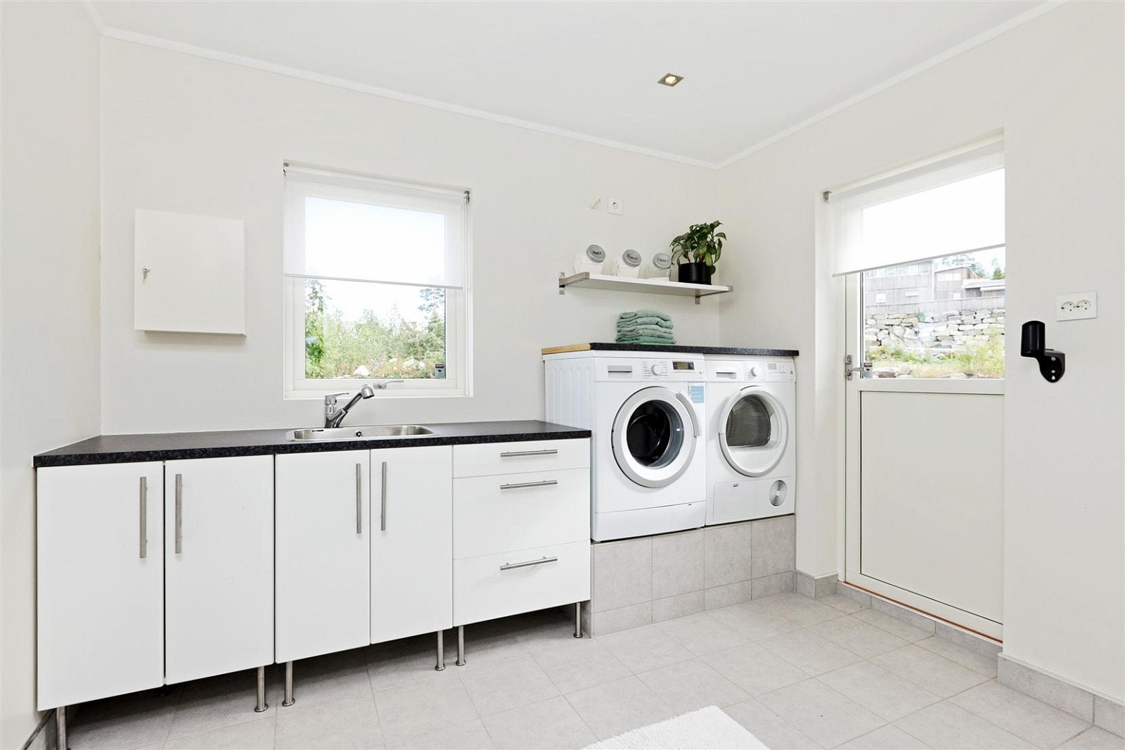 Romslig vaskerom med flislagt gulv og egen utgang til uteområdet på framsiden av boligen. Hvit skap innredning med benkeplass og oppvaskkum. Stor vv.bereder på hele 300 liter, og downligts i tak. Galleribilde