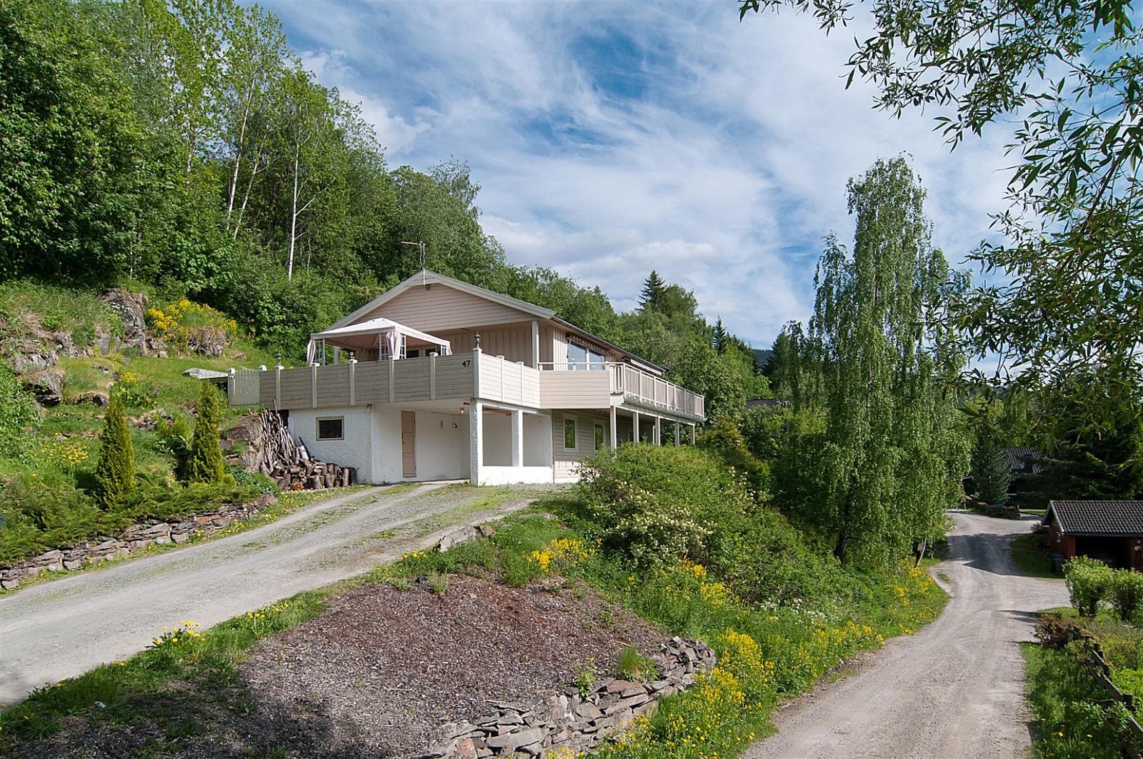 Tomten er planert rundt huset, opparbeidet hage med plen og beplantninger, ellers naturtomt med gress og fjell, også noen trær på tomten. Gruset adkomst fra rolig boliggate i bakke opp til gruset gårdsplass foran inngangspartiet og carport. Galleribilde