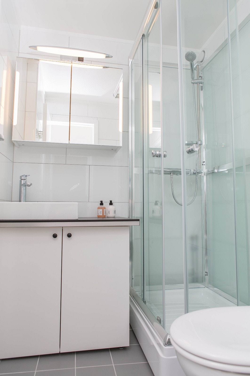 Flislagt Bad med dusjkabinett, servant, overskap med speil og vegghengt toalett. Galleribilde