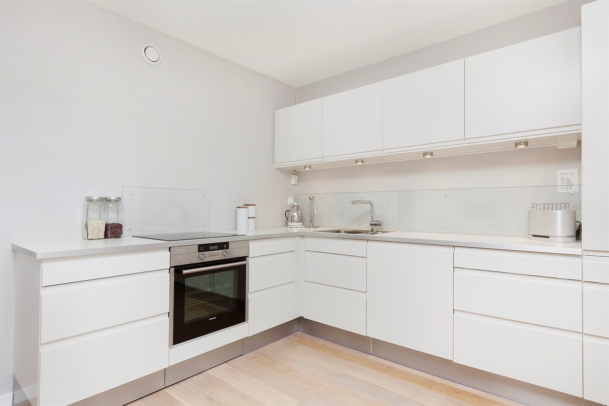 Stilrent HTH-kjøkken med integrerte hvitevarer og åpen løsning mot stue Galleribilde