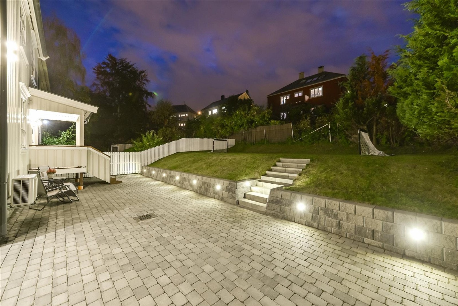 Påkostet gårdsplass som er belagt med belegningsstein. De innfelte lyspunktene lager en fin ramme rundt eiendommen. Galleribilde