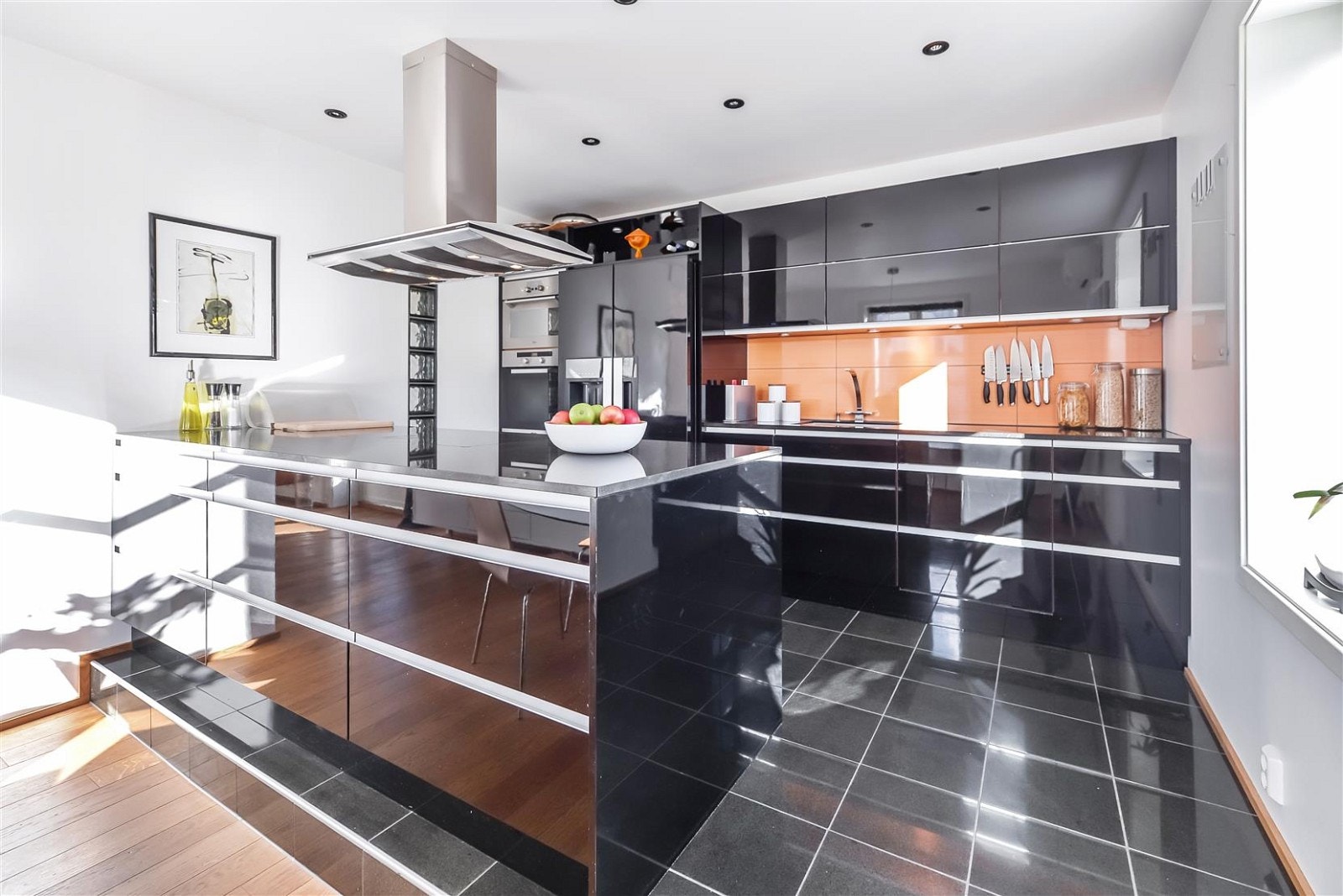 Lekkert og påkostet kjøkken fra JKE Design med svart granittplate og flislagt gulv med varmekabler. Galleribilde