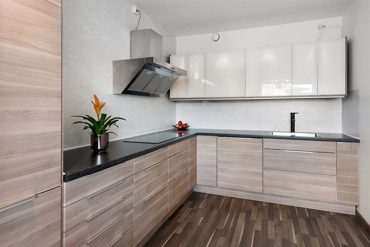 Kjøkkenet er moderne og stilfullt, samt praktisk designet med god benke- og lagringsplass. Innredningen har lysebrune, glatte fronter med vitrineskap og benkeplate i mørk laminat med enkel vaskekum og keramisk koketopp. Galleribilde