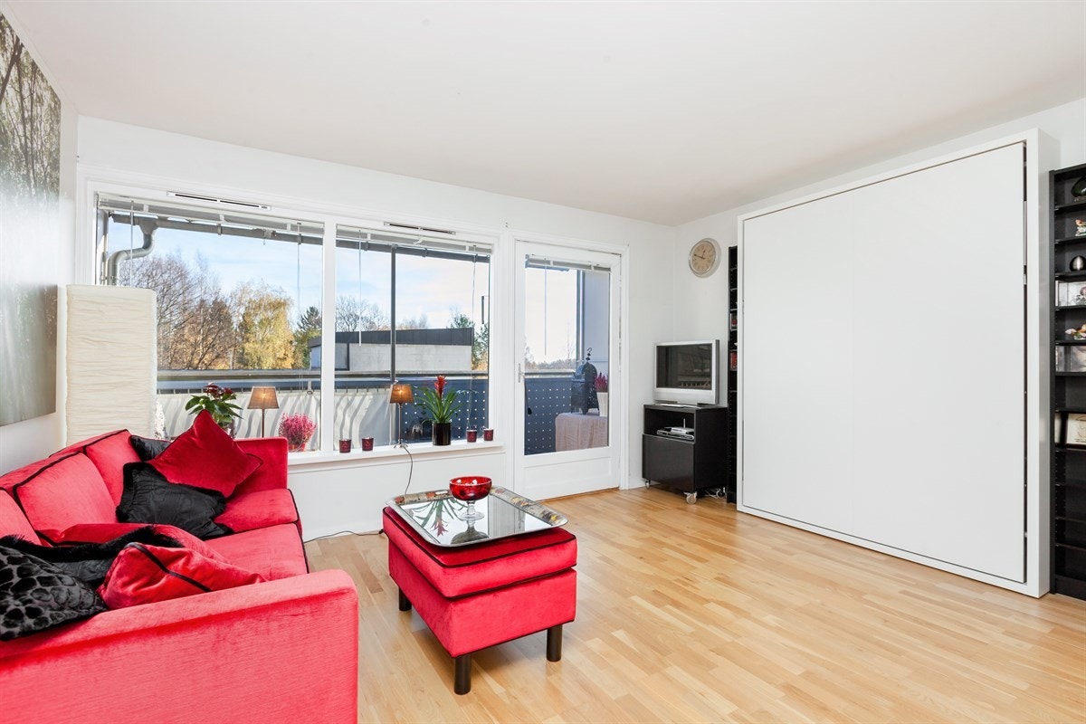 Lys og trivelig stue med utgang til balkong. Det er montert praktisk sengeskap på veggen som om ønskelig kan kjøpes av ny eier Galleribilde