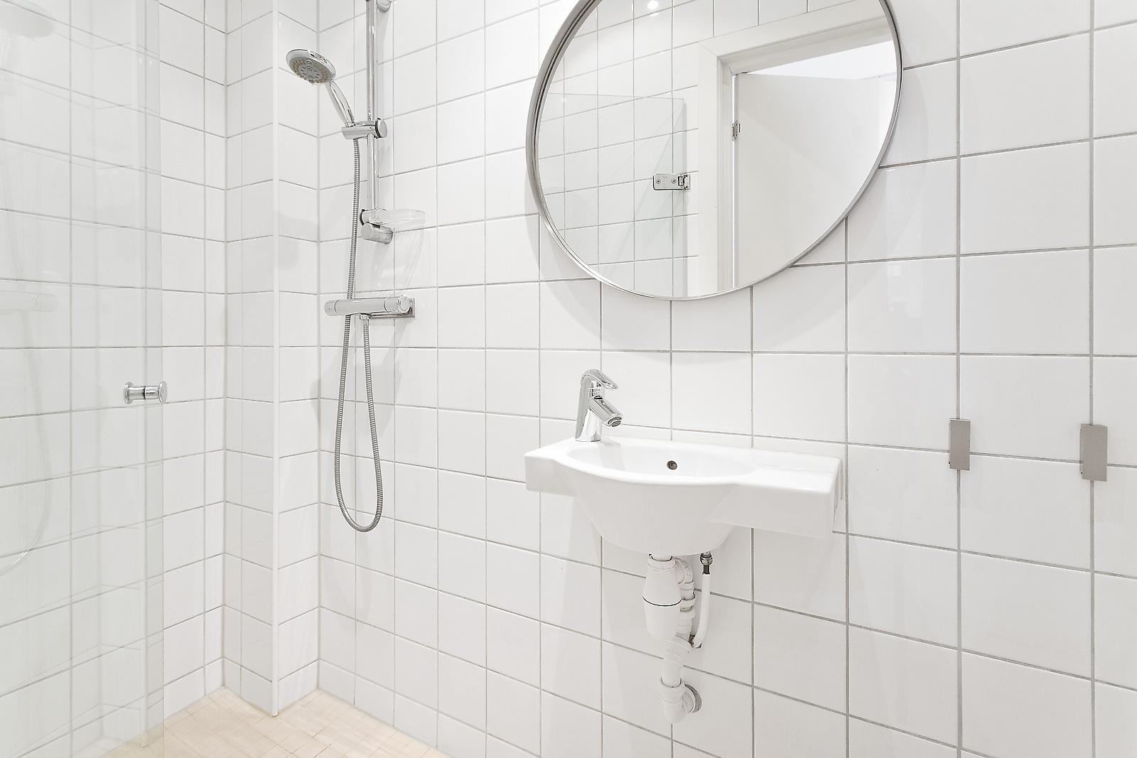 Pent flislagt baderom med veggmontert wc, dusjplass med glassdør. Plasseffektiv servant. Innfelte hyller i vegg. Gulvvarme. Galleribilde