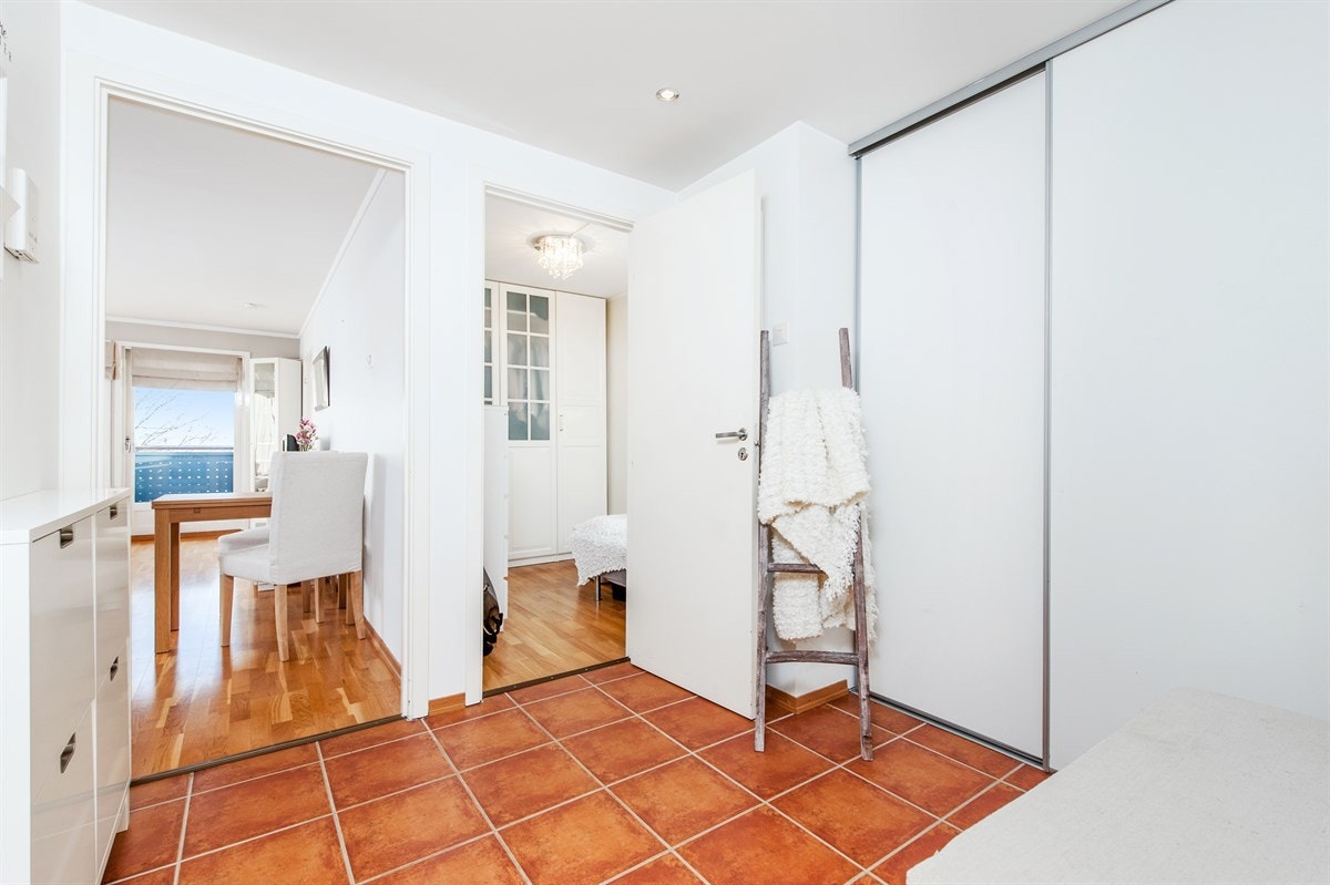 Romslig, flislagt entrè med stor skyvedørsgarderobe og downlights i himling Galleribilde