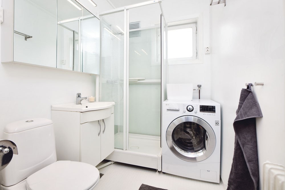 Bad med dusjkabinett, servantskap og kombinert vaskemaskin og tørketrommel. Galleribilde