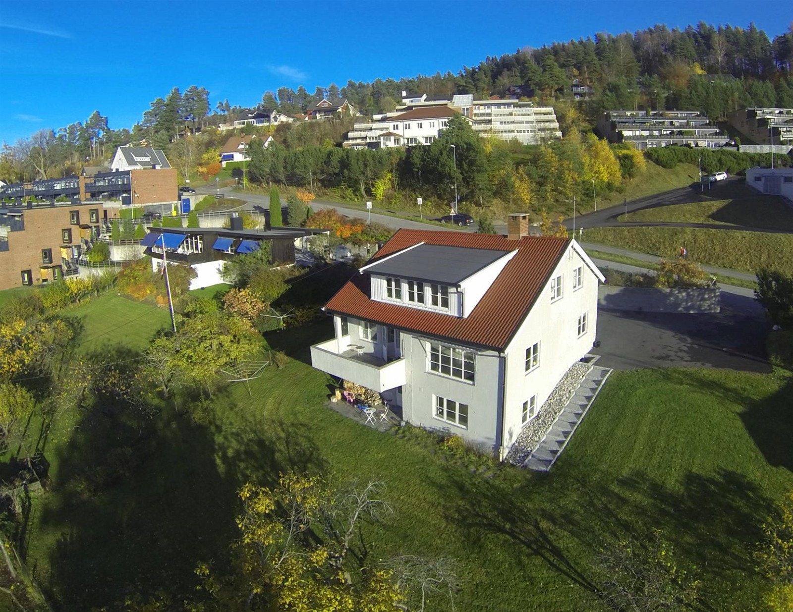 Pent opparbeidet tomt med nyasfaltert gårdsplass og oppmurt naturstein mot veien. Hagen er lett skrånende og består av plen og noen få trær. Galleribilde