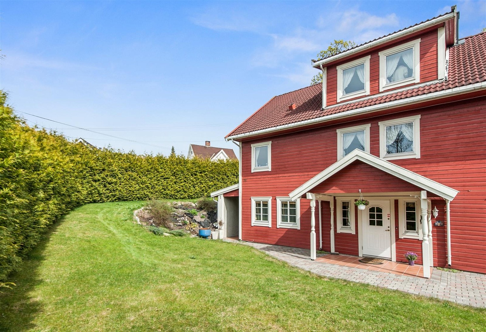 Inngangspartiet og adkomsten er med belegningssten samt grønne partier med gressplen, busker og annen beplantning. Galleribilde