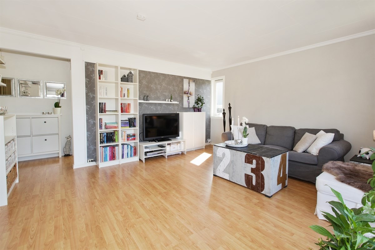 Lys og pen stue med god plass til sofagruppe og tilhørende møblement. Store vindusflater slipper inn rikelig med sollys. Fondveggen bryter fint mot de ellers lyse overflatene Galleribilde