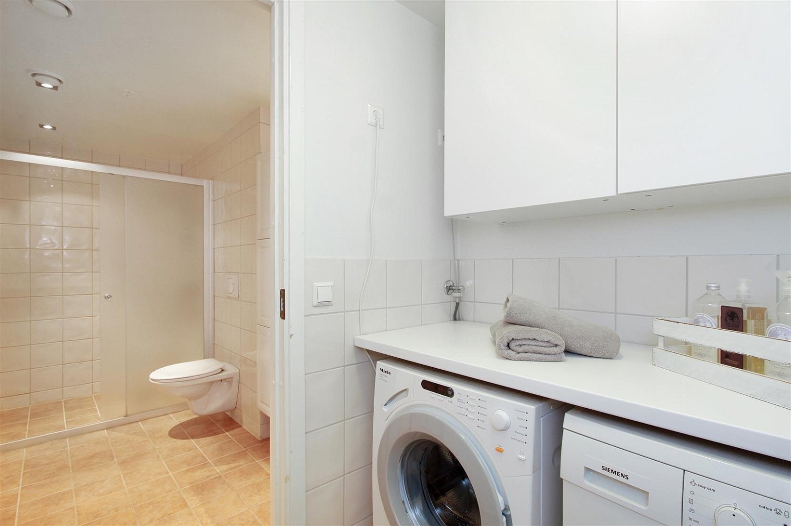 Det er eget vaskerom med parktiske skap på vegg og arbeidsbenk med plass til vaskemaskin og tørketrommel under Galleribilde