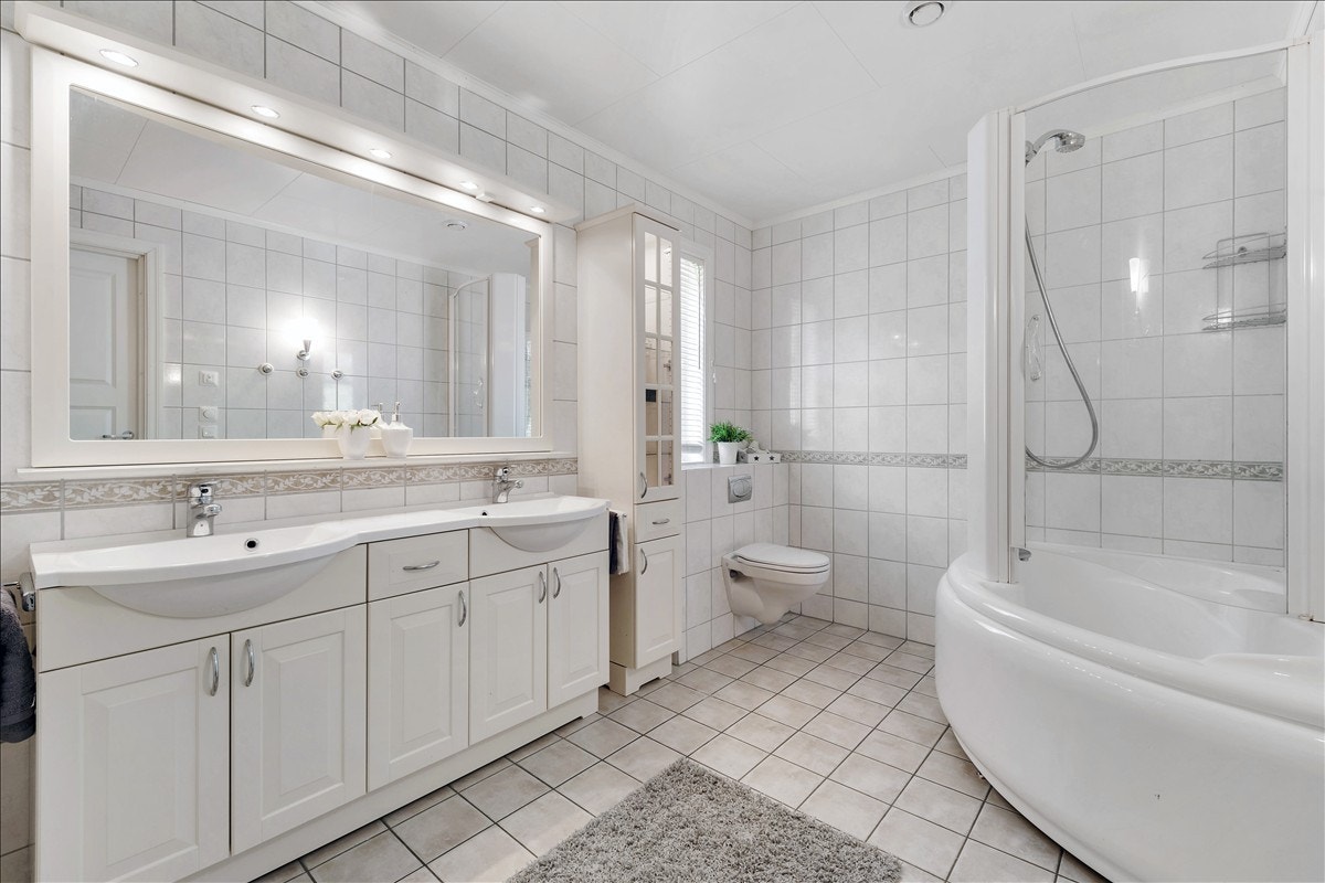 Flislagt bad, med dobbelservant og mye oppbevaringsplass i innredningen, vegghengt wc og et smart hjørnekar med dusjvegger. Galleribilde