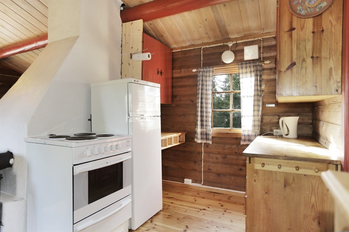 Fra stue er det åpent inn til et enkelt kjøkken med heltre dører, komfyr og kjøl-/fryseskap. Galleribilde
