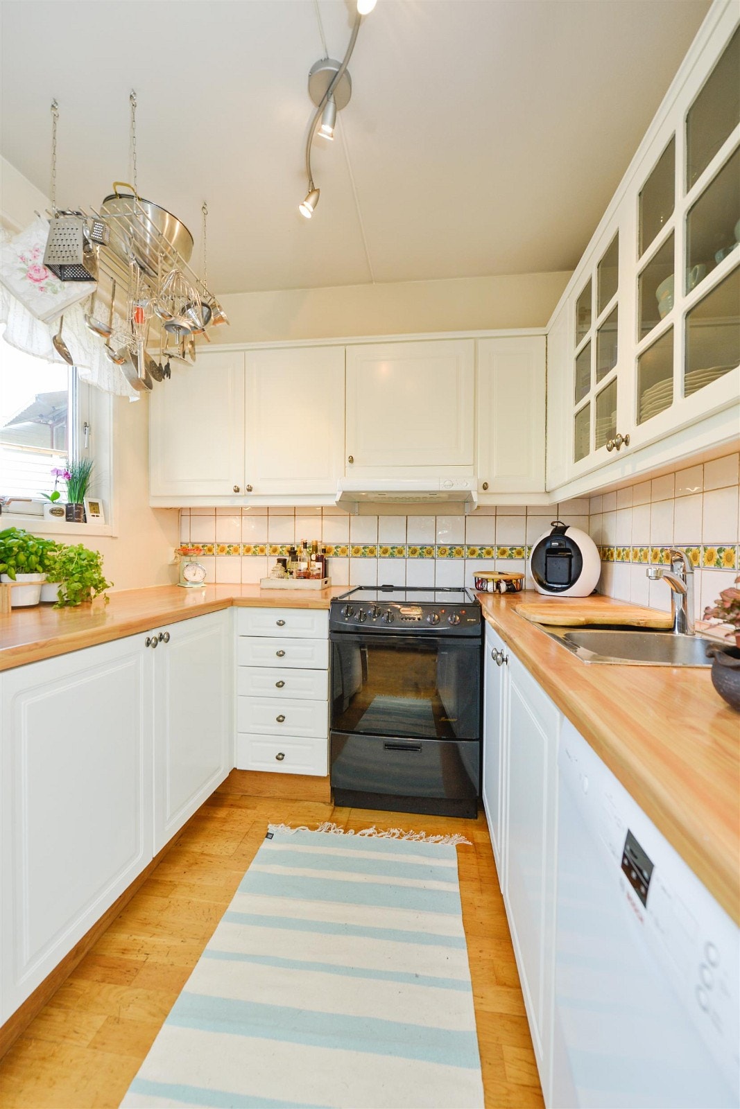 Delvis åpent kjøkken mot spisestuedelen med god skapplass. Hvite, nymalte fronter i profilert utførelse, fliser over kjøkkenbenk og laminat benkeplate. Galleribilde