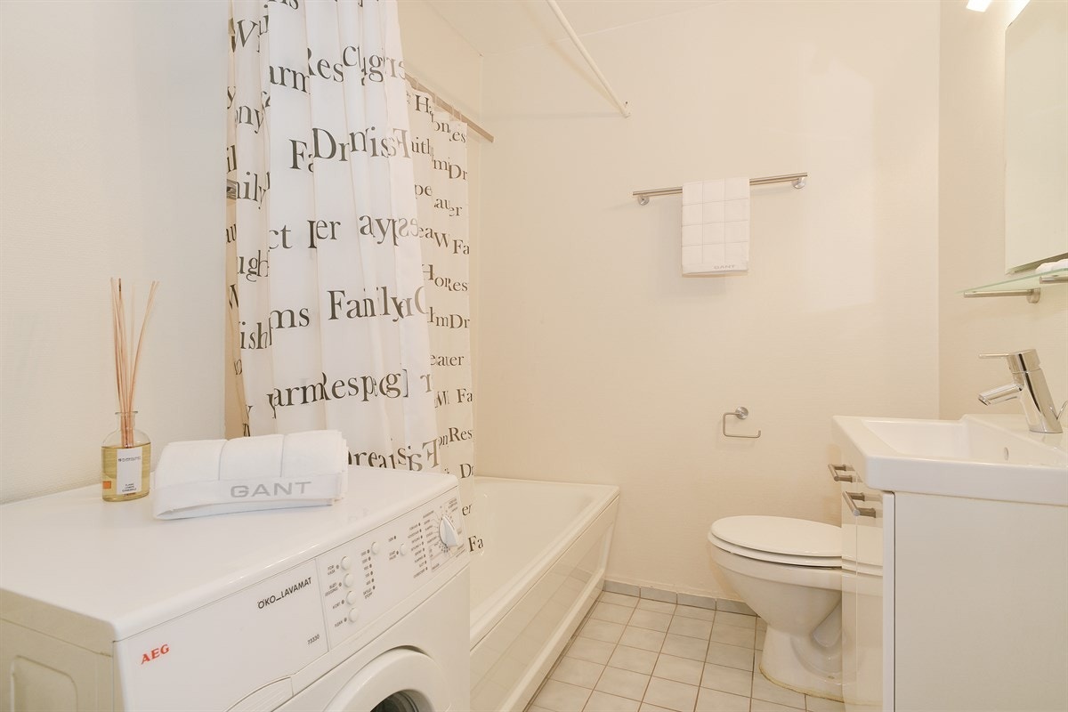Badet er praktisk med fliser på gulv og har badekar med dusjforheng, tørkeskap og opplegg for vaskemaskin. Galleribilde