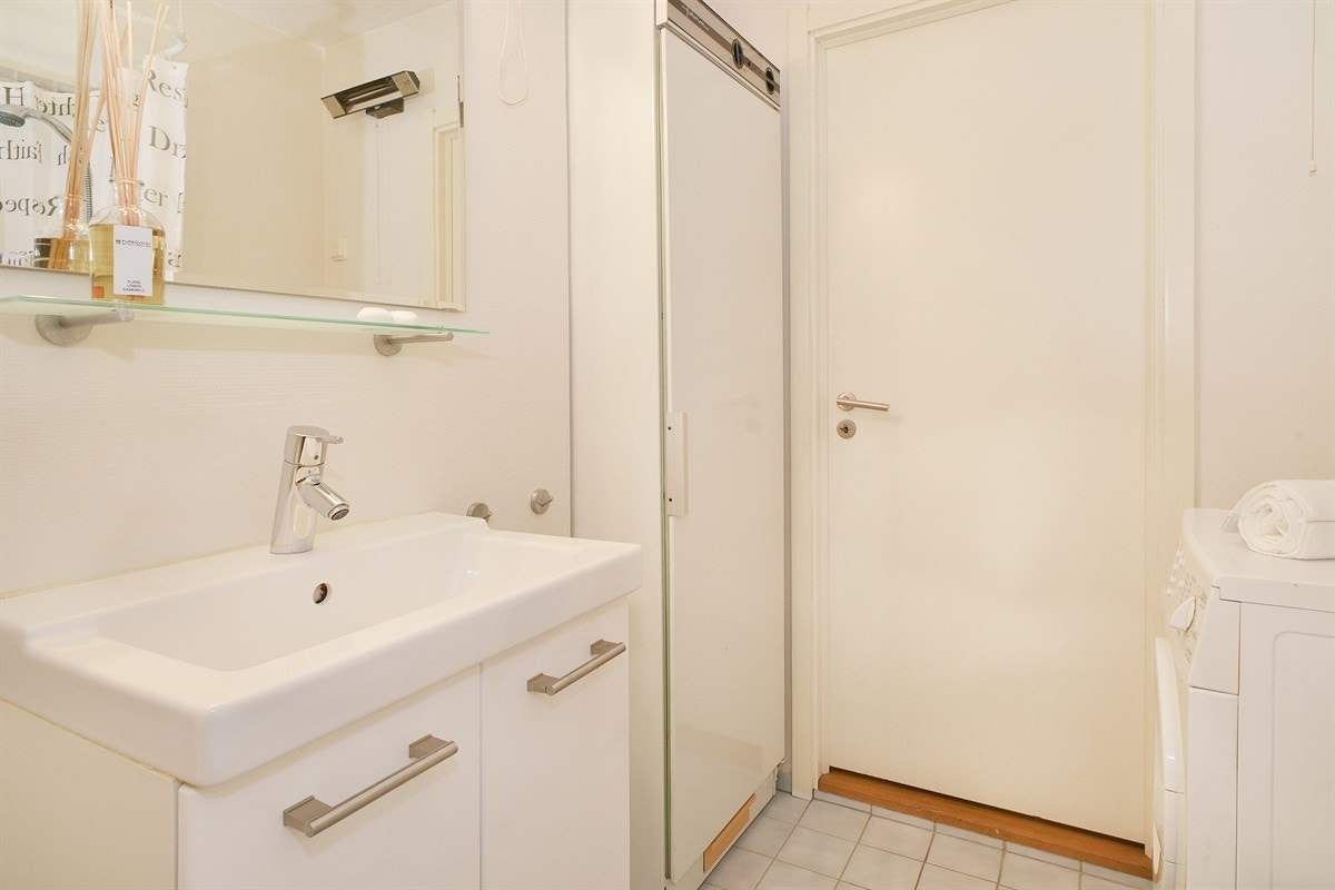 Det er baderomstapet på vegg, frittstående toalett, servantskap med heldekkende servant og belysning over speil. Galleribilde