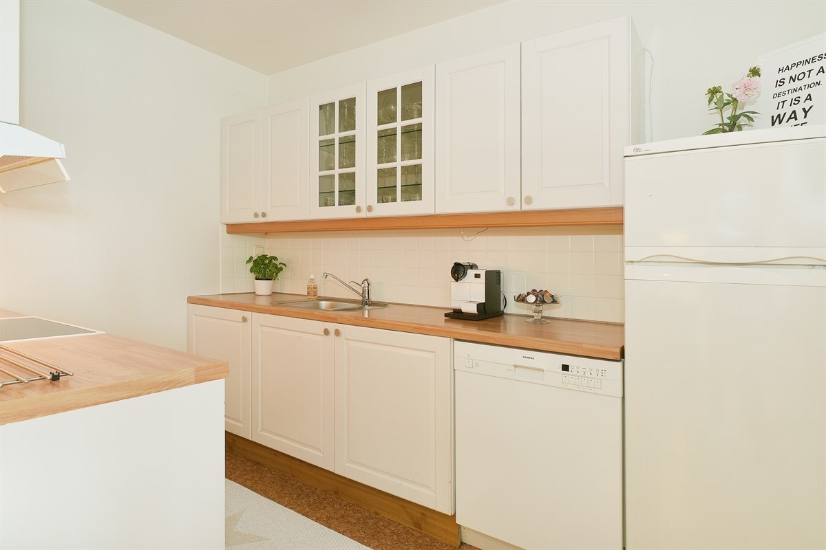 Videre har kjøkkenet fliser over laminert benkeplate med dobbel vaskekum, opplegg for oppvaskmaskin og nisje for kjøleskap. Galleribilde