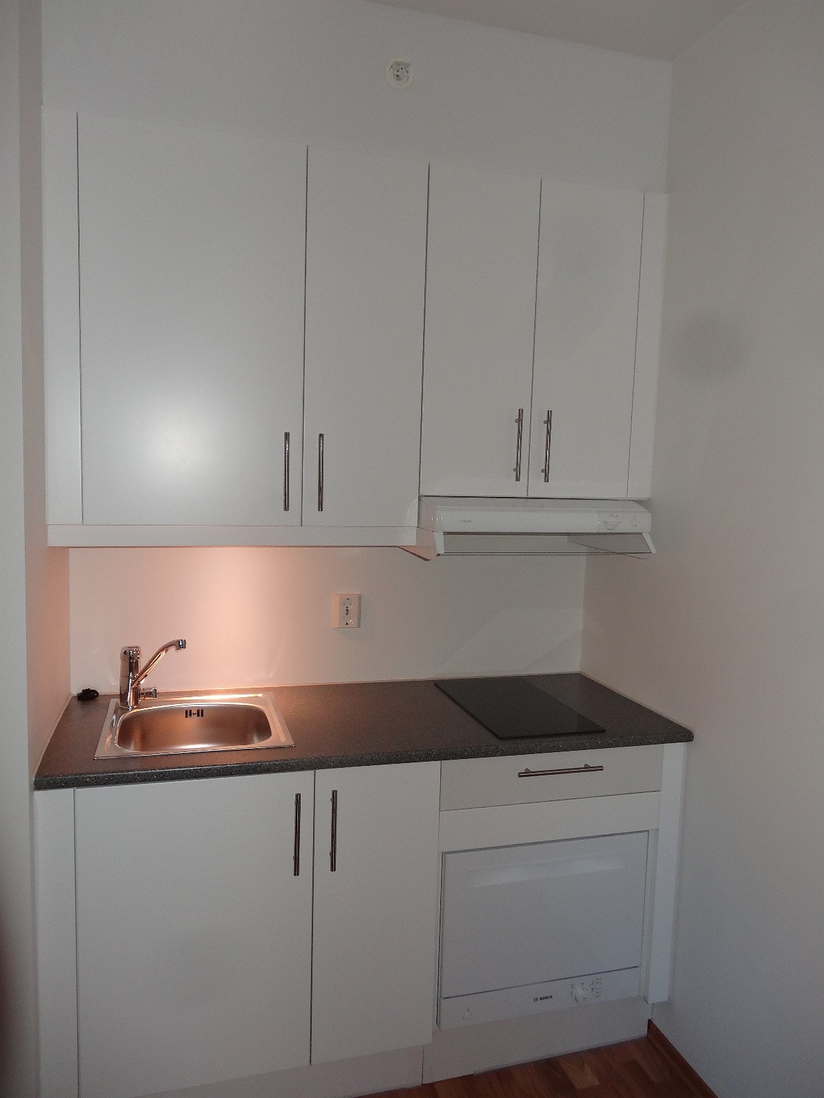 Kjøkkenet har nye integrerte hvitevarer. Induksjonstopp, ovn, laminat benkeplate, ventilator og hvite, glatte fronter. Galleribilde