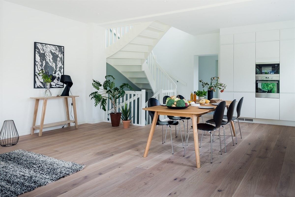 Kjøkkeninnredningen er plassert langs stuens ytterkant og henvender seg åpent mot gulvflaten i forkant der store møbelgrupper som et spisebord og en salong finner sin plass. Galleribilde