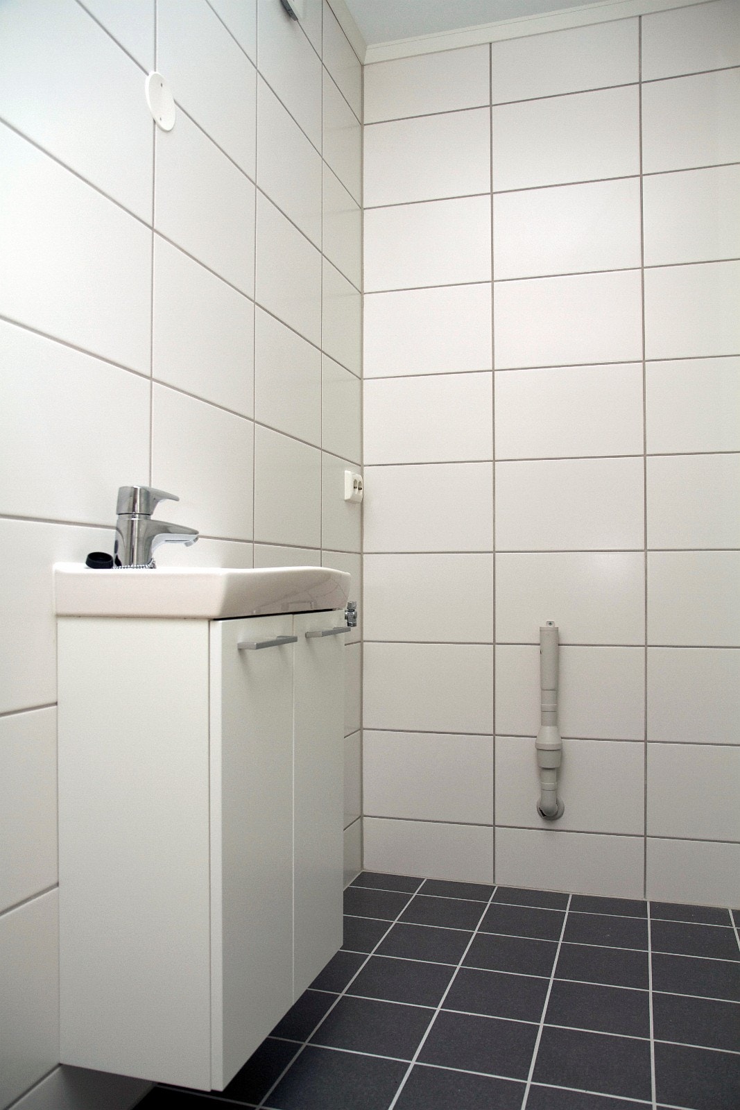 Flislagt bad med vegghengt toalett, dusj med slagdører og opplegg for vaskemaskin Galleribilde