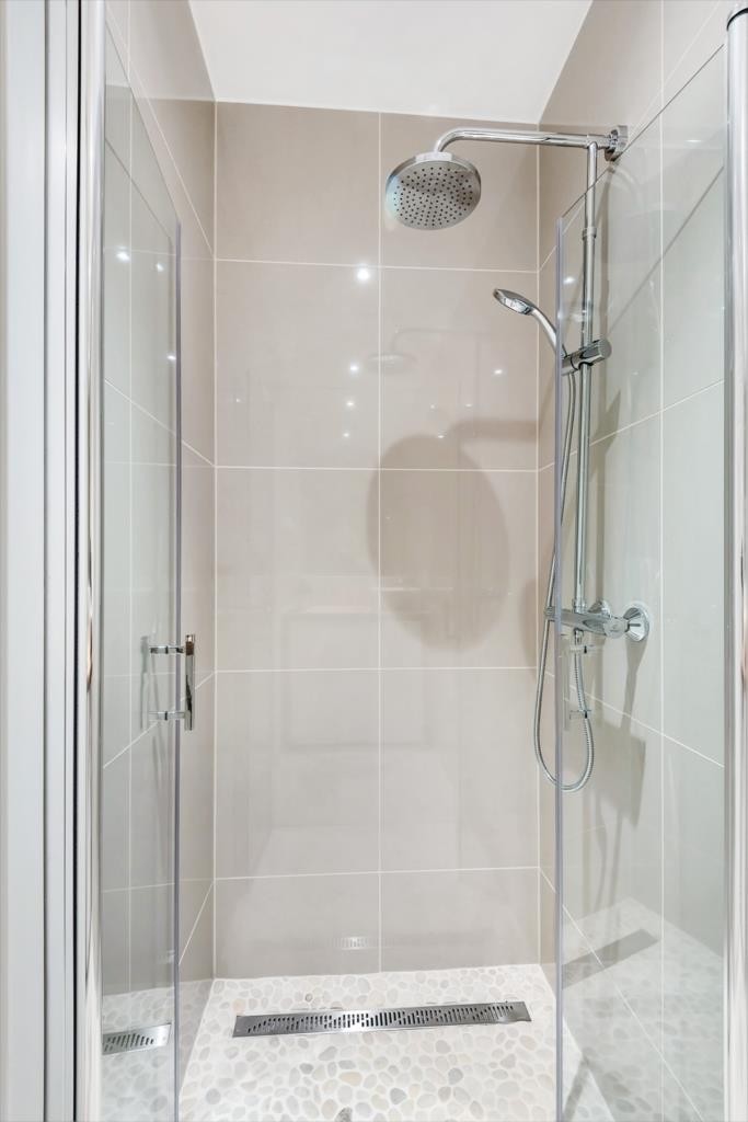 Romslig dusjnisje med rullestein på gulv og moderne metersluk. Innfellbare dusjvegger i herdet glass. Pen dusjgarnityr med vannfallsdusj. Galleribilde