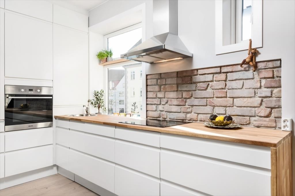 Stilren fritthengende ventilator i børstet stål med belysning, over innfelt teglstein bak glassvegg. Galleribilde