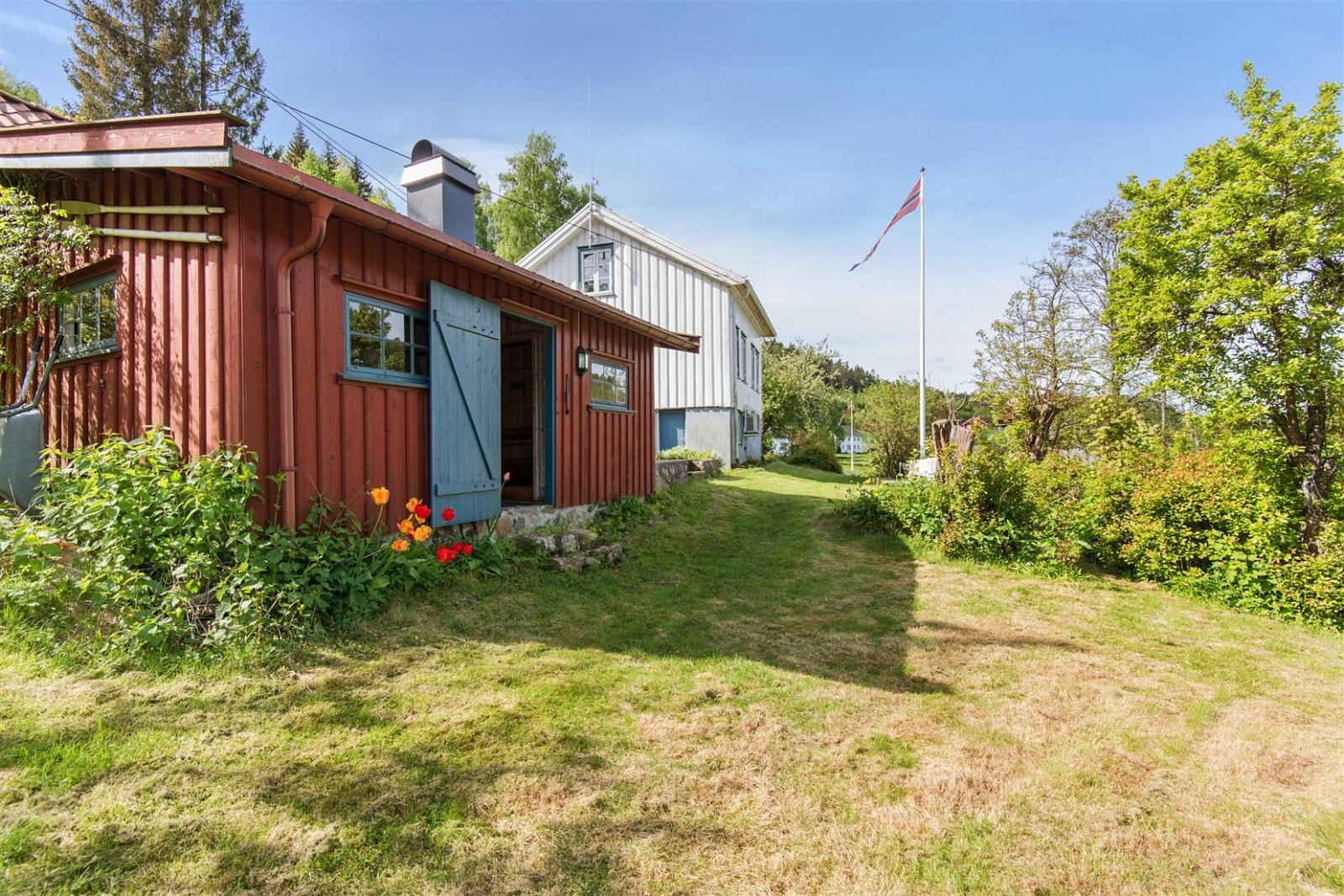 Tomten er skrånende, delvis innrammet med statikkgjerde og har stort, plenlagt område, syrintre, frukttrær og flaggstang. Galleribilde