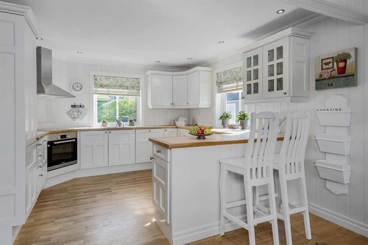 Kjøkkenet fra kvalitetsleverandøren JH interiør er elegant og holdt i en klassisk stil, samt praktisk designet med god benke- og lagringsplass. Innredningen har hvite, profilerte fronter med vitrineskap, og heltre benkeplate med nedfelt vaskekum. Galleribilde