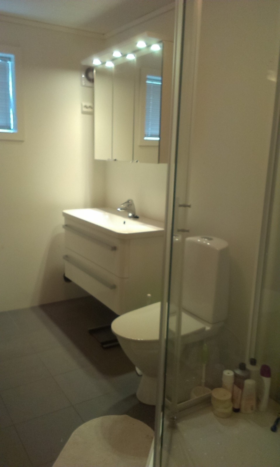 Bilde fra bad med servatnt med skap og speil, WC og dusjkabinett. Fliser og varmekabler på golvet. Galleribilde