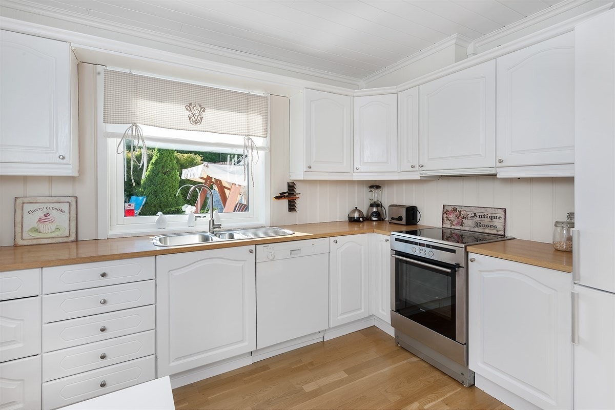 Delikat kjøkken med god lagringsplass i skuffer og skap, hvor frontene er hvitmalte og profilerte. Videre har kjøkkenet benkebelysning over pen benkeplate med dobbel vaskekum, oppvaskmaskin og plass for komfyr og kjøl/frys. Galleribilde