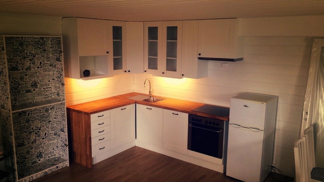 Kjøkken med komfyrvakt. Spisestue ved siden av. Det står nå et større kjøleskap i rustfritt stål der. Galleribilde