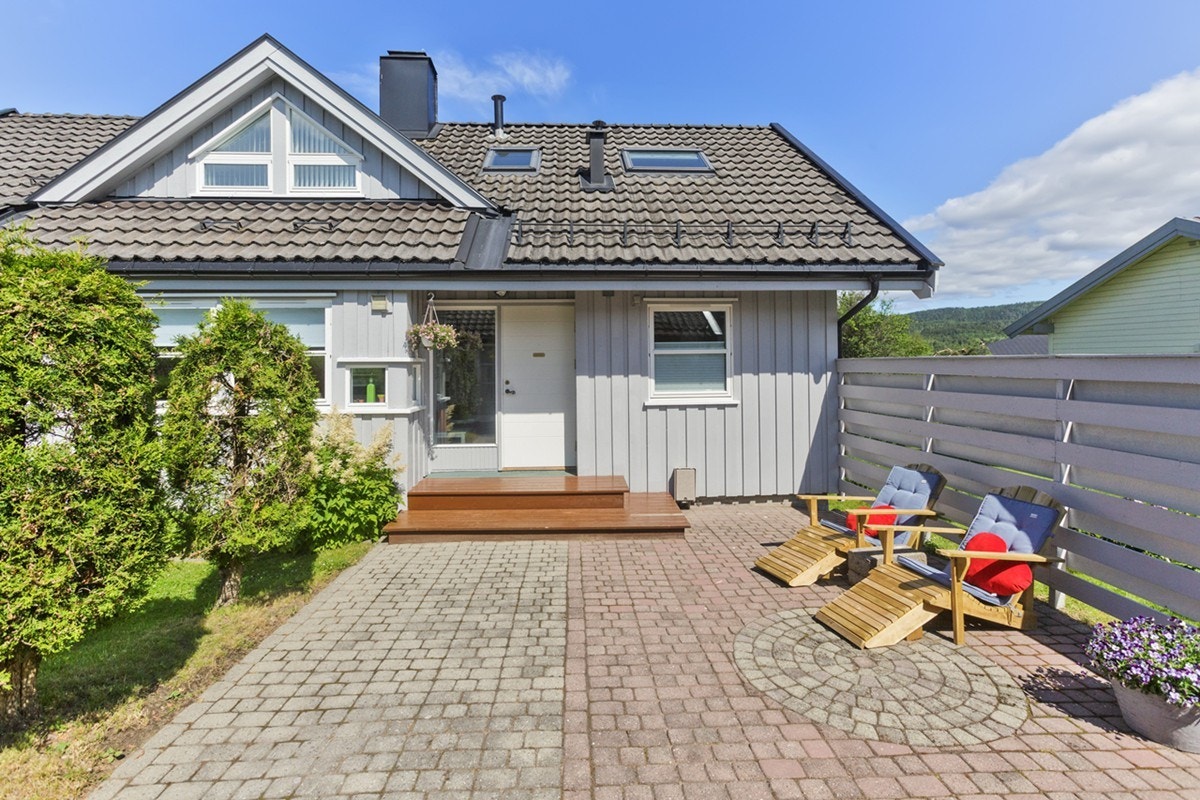 Fasade inngangsparti. Brostein er pent belagt, med plass til utemøbler. Skjerming mot naboen og stort vindu i entré som gir dagslys inn. Galleribilde