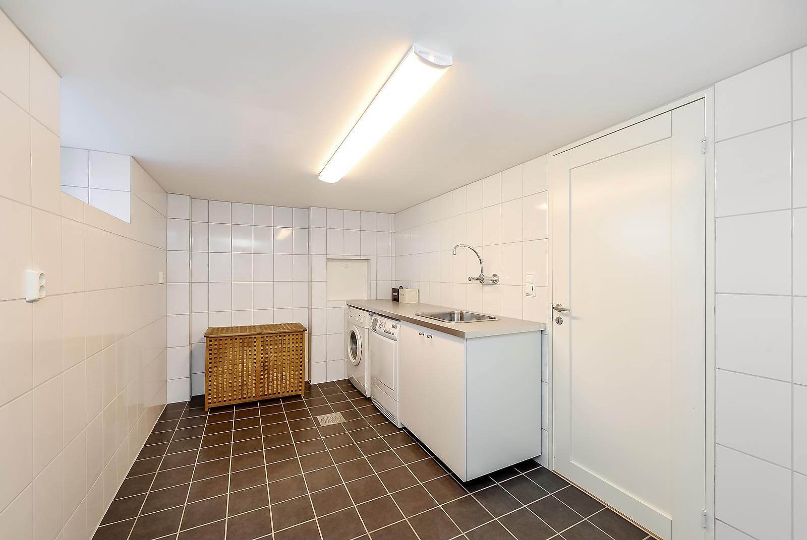 Vaskerommet i kjelleren. Legg merke til den praktiske innredningen med vaskemaskin og tørketrommel under benkeplate. Vask og skapplass. Galleribilde