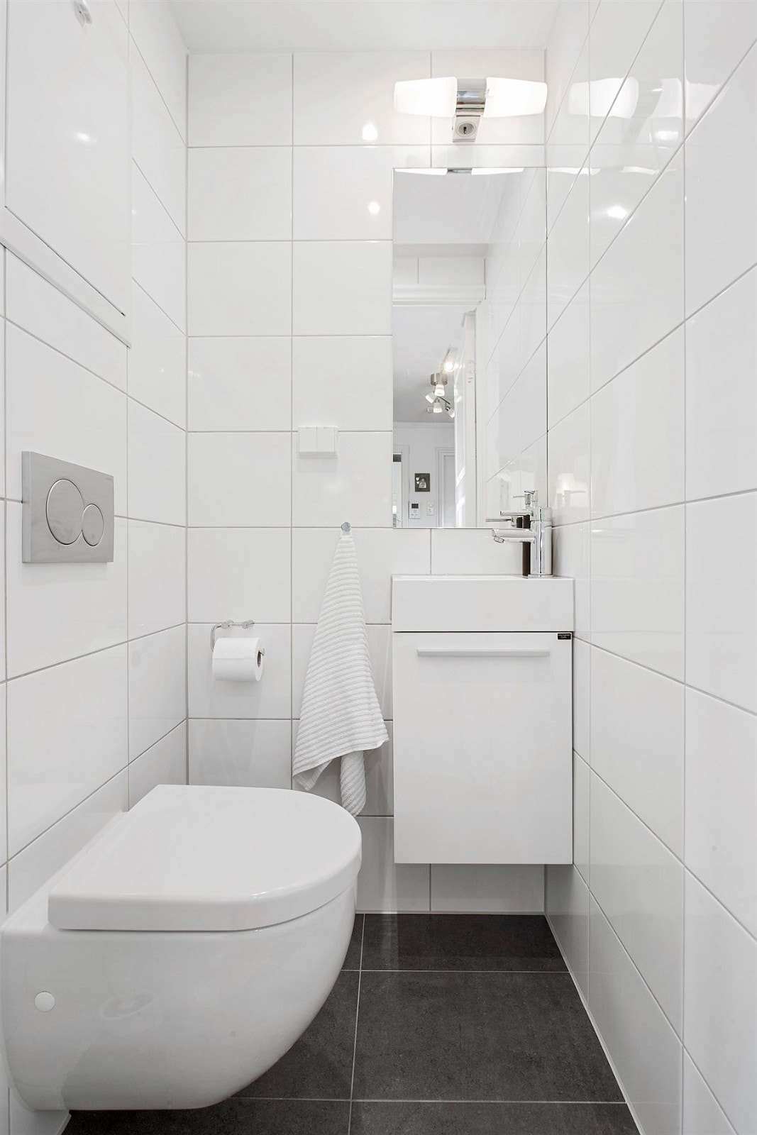 Separat wc er holdt i samme stil med mørke fliser på gulv, hvite fliser på vegg og downlights belysning. Innredningen består av veggmontert toalett, servant på hvitt servantskap, speil med vegglampe og stikk. Galleribilde