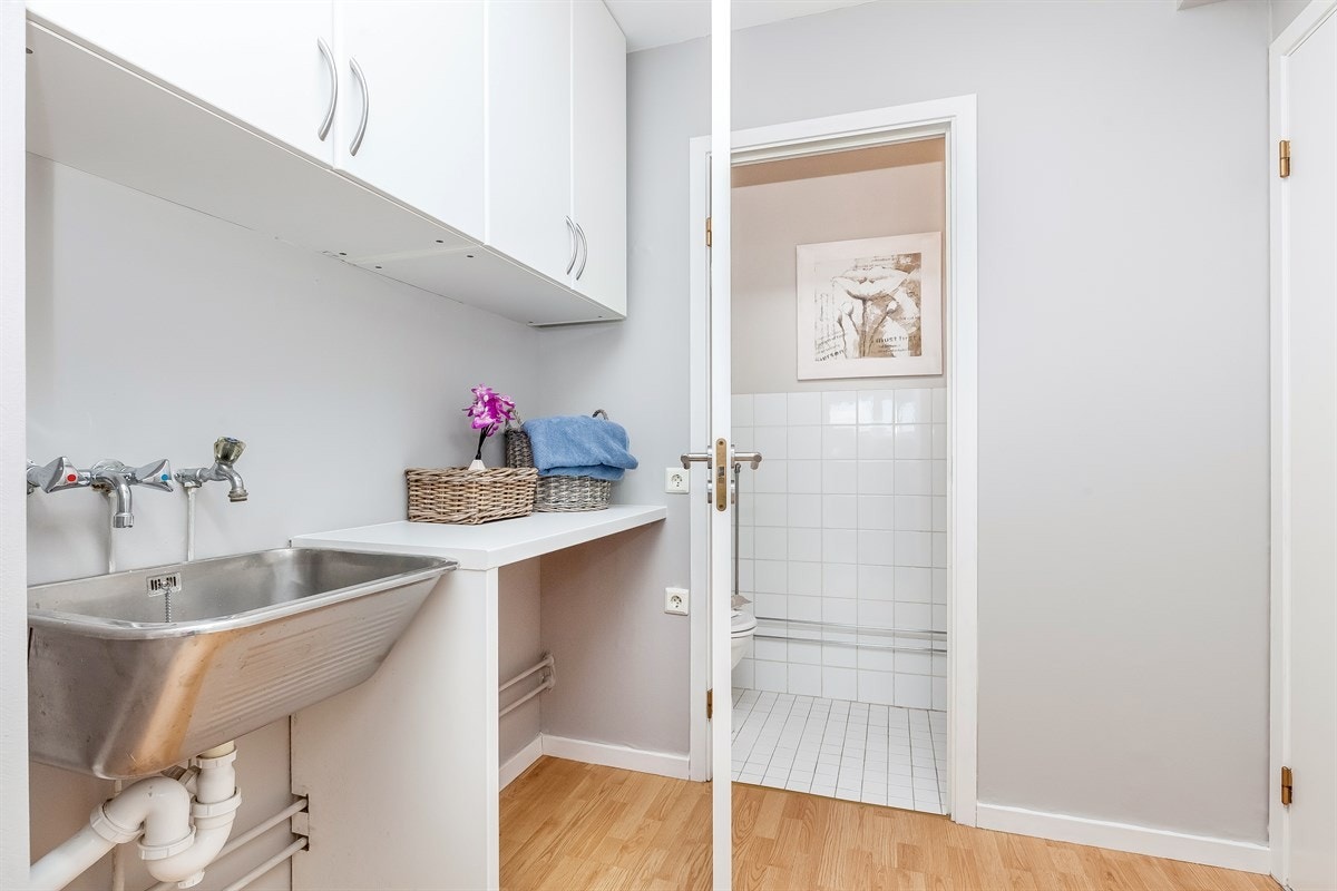 Praktisk vaskerom innredet med utslagsvask, vaskebenk og overskap. Inngang til separat wc. Galleribilde