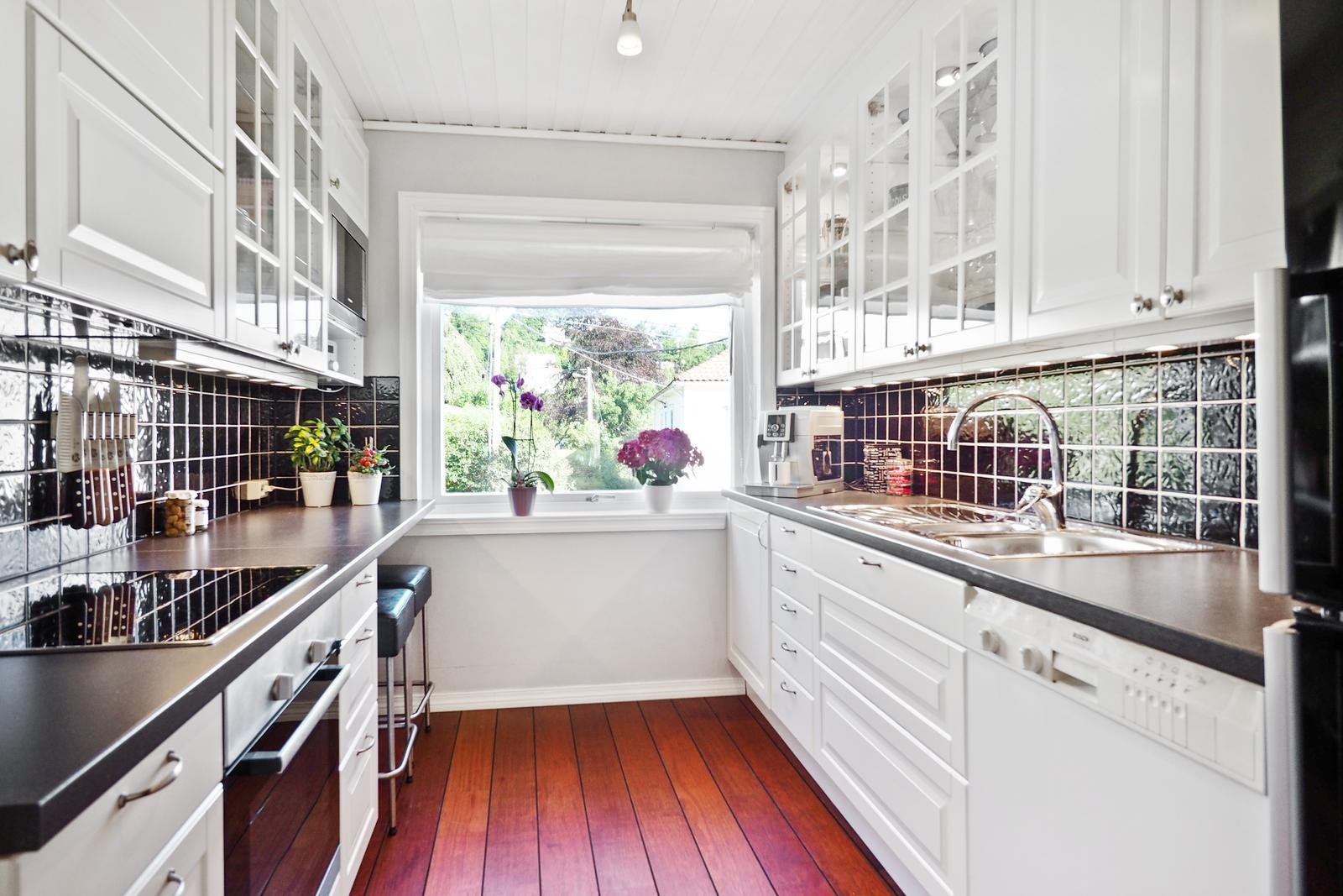 Videre inn får du kjøkkenet med en hvit og lys kjøkkeninnredning med takhøye skap som gir godt med oppbevaring. Flere skap er innredet med lys som gir en fin atmosfære. Galleribilde