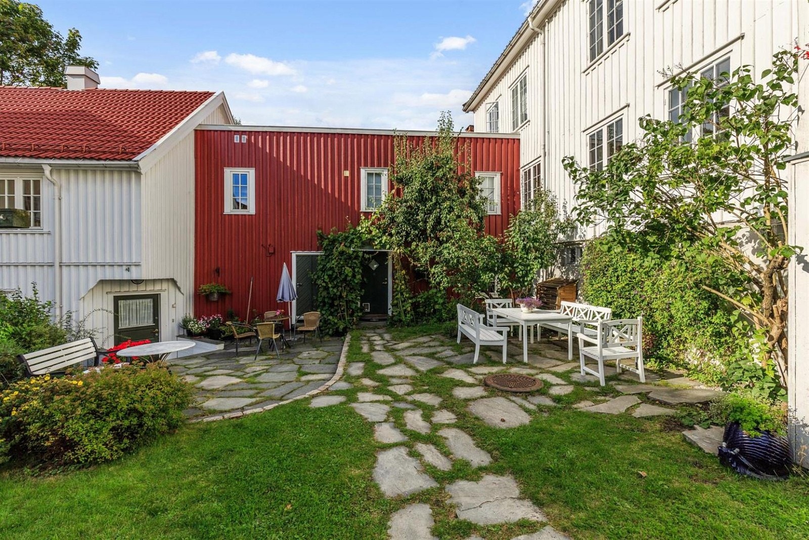 Den sjarmerende uteplassen som viser sameiets 3 bygninger hvor hovedleiligheten er plassert i hvoedhuset til høyre på bildet og hybelleiligheten i mellombygget. Galleribilde