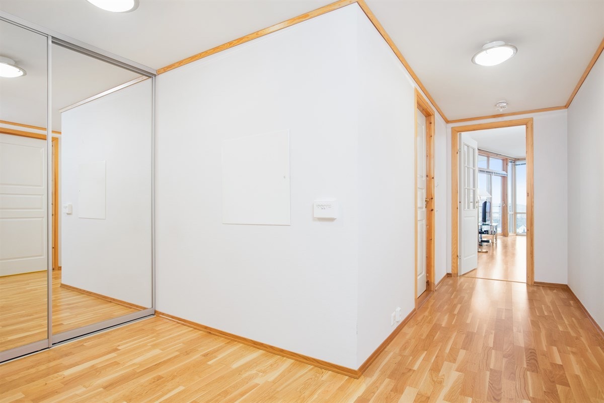 Man ønskes velkommen inn i en åpen og luftig gang. Gangen fører deg til soverom, bad og glassdør mot kjøkken/stue og utsikt. Langs den ene veggen er det integrert et takhøyt garderobeskap med speilskyvedører. Galleribilde